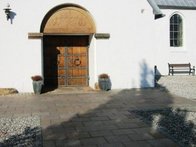 Granitfliser omgivet af perlesten foran indgang til hvid kirke med dobbeltdør og dekorativ bue over.