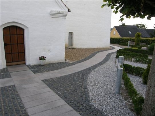 Aflange fliser lagt som stier hen til kirke og omkranset af brosten.