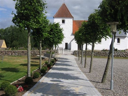 Træer langs allé af fliser, som fører op til kirke.