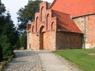 Sti af betonfluser og chaussésten, som fører op til rødmuret kirke.